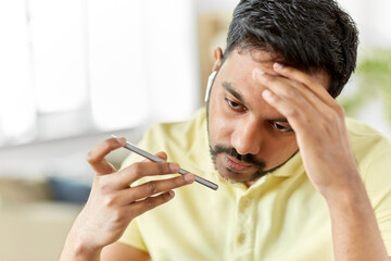 technology, communication and emotions concept - close up of stressed indian man with earphones calling on smartphone or using voice command recorder