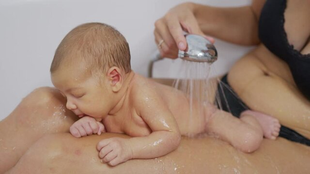 Newborn baby girl is taking bath in bathroom at home. Hygiene and health care for newborn baby.