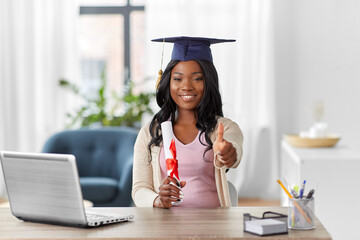 e-learning, education and people concept - happy smiling african american female graduate student with laptop computer and diploma showing thumbs up at home