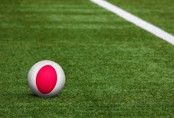 Japan flag on ball at soccer field background. National football theme on green grass. Sports competition concept.