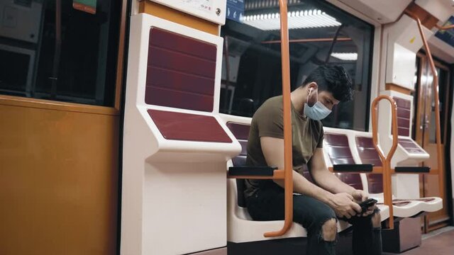 Caucasian man in olive shirt with green backpack with mask touching his iPhone in Madrid metro