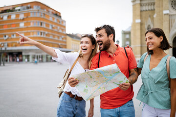 Holidays, travel, friends and tourism concept. Happy friends looking into tourist map in the city