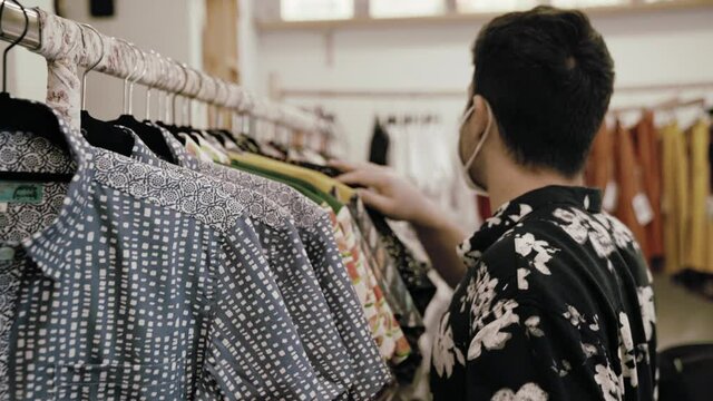 Hombre caucásico con camisa vintage comprando ropa en una tienda de ropa vintage con mascarilla covid coronavirus