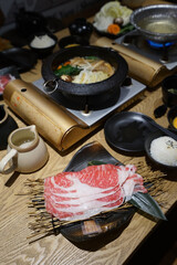 Wooden table fulled of vegetables, Sliced Wagyu beef and pork, rice ,raw egg and dipping sauce- Sukiyaki (Japanese hot pot)