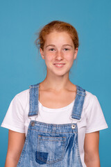 Shot of a smiling teenager redhead girl   against  blue background in the studio