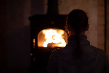 A young introvert girl sits at home by the fireplace in the evening and watches the fire. Reading...
