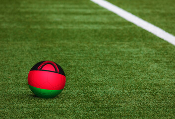 Malawi flag on ball at soccer field background. National football theme on green grass. Sports competition concept.