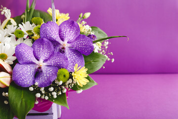 Beautiful bouquet of flowers in lilac basket on purple background with copy space. Orchids, lilies, chamomiles floral floristic composition. Greeting card for romantic date, valentine day, 8 March