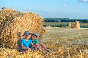  Children  sit at a haystack in a field with hay bales after harvest on a sunny day and have fun talking