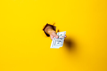 Woman's hand holds a bundle of one hundred dollar bills on a yellow background