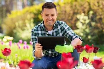Fototapeta premium gardening and people concept - happy smiling middle-aged man with tablet pc computer and flowers at summer garden