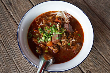 Close up bowl of Thai rice noodles with spicy pork sauce served on wooden table- Classic Northern Thailand recipe