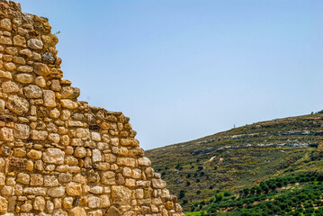 Remains of a sandstone fortress wall on the sky and a hill with terraced agricultural plantings