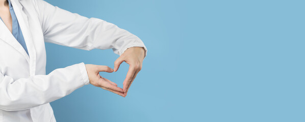 Obraz na płótnie Canvas Female doctor in white uniform forms a heart shape with her hands. Minimal blue background. Banner with copy space. Heart, cardiology and medical care support and assistance and love