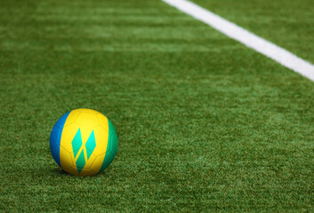Saint Vincent And The Grenadines flag on ball at soccer field background. National football theme...