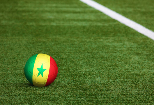 Senegal flag on ball at soccer field background. National football theme on green grass. Sports competition concept.