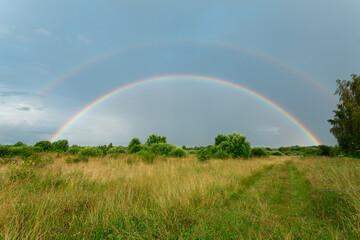 Summer field with double rainbow after the rain. Horizontal image.