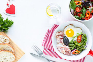 Breakfast for your beloved for the holiday: heart-shaped egg, bacon, green beans on a white table. Selective focus. View from above. Copy space
