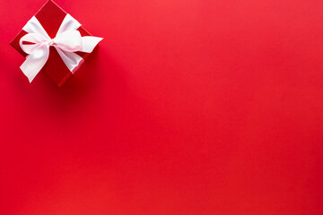 Gift box with white bow on red background, top view with copy space