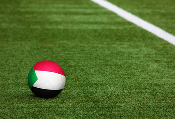 Fototapeta na wymiar Sudan flag on ball at soccer field background. National football theme on green grass. Sports competition concept.