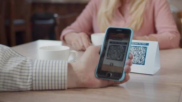 Close up of customer using digital mobile phone scan QR code paying for buying coffee in modern cafe