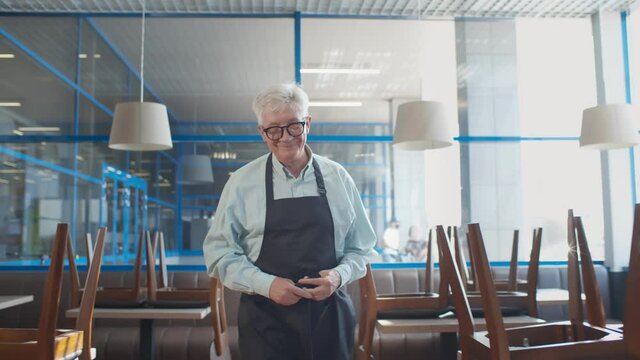 Mature small business owner arranging apron walking in closed cafe