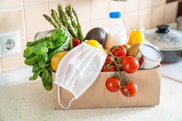 Safe food delivery concept - groceries in box with medical mask , kitchen background