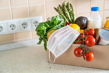 Safe food delivery concept - groceries in box with medical mask , kitchen background