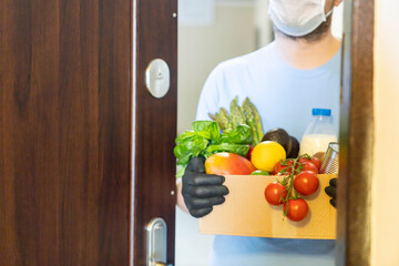 Safe food delivery concept - delivery man holds gloceries wearing medical mask and gloves