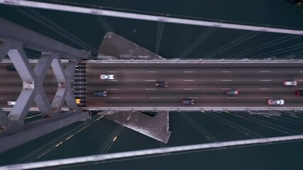 Cinematic industrial shot. 4K aerial top down over the busy city road at night time. Cars are driving with turned head lights by multi-laned modern suspension bridge illuminated in the dark, USA - Powered by Adobe