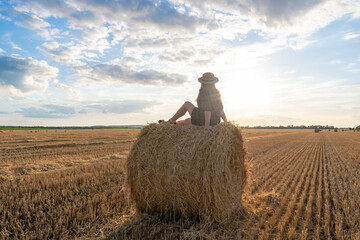Naklejka na ściany i meble Girl at sunset in a field with hay.