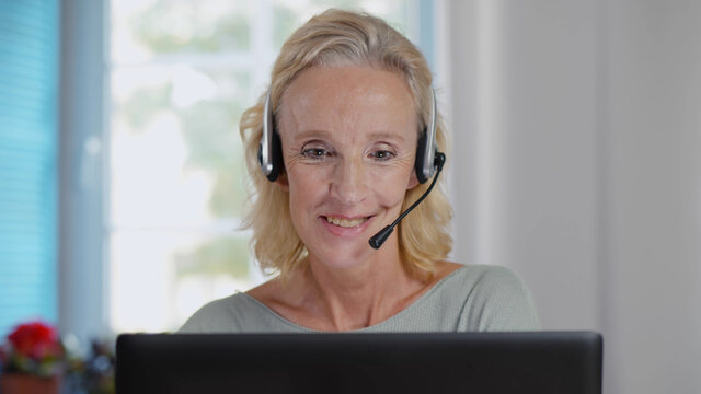 Happy Mature Telemarketer Woman With Laptop Attending Call With Headset