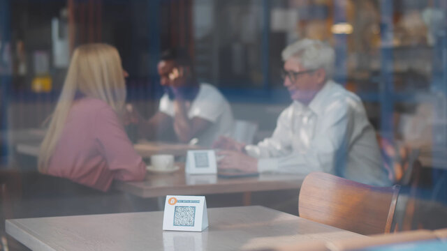 View through window of waiter putting sign with qr code for discount or contactless payment on table