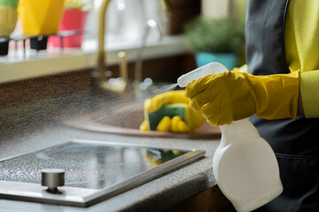 Close up person in yellow rubber gloves cleaning house, wipes kitchen worktop using spray detergent, washes induction stove with sponge. Housework cleaning service, household chores, copy text space