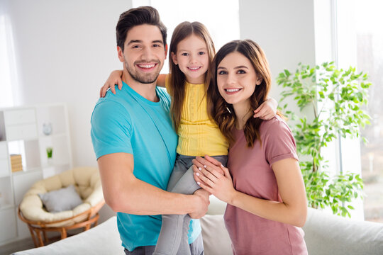 Photo of idyllic three people mommy daddy carry small kid daughter enjoy gentle bonding emotions hug embrace in house indoors