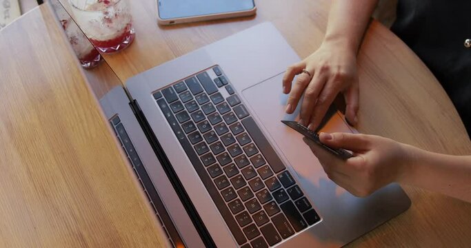 Young woman sitting on the coffeeshop, using laptop computer for online shopping with black platinum credit card on cafe background. 
