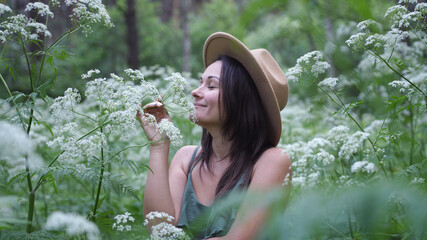 Young pretty woman in hat poses in deep forest among white flowers.