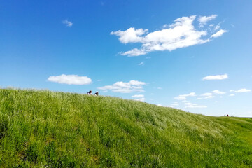 Green hill and blue sky. Two little figures on the top of a green hill on a sunny summer day. White clouds in the blue sky.