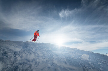 Naklejka na ściany i meble Athlete male skier jumps from a snow-covered slope against the backdrop of a mountain landscape of snow-covered mountains on a sunny day. The concept of winter sports wide angle