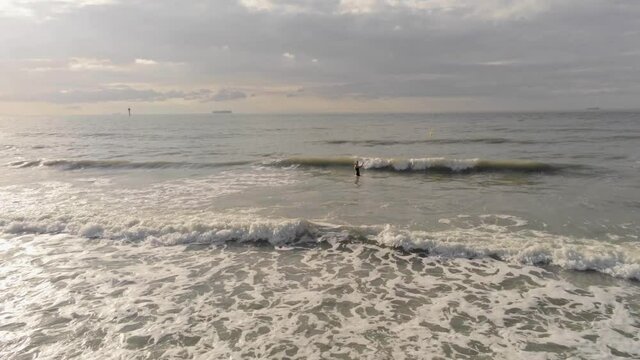 Aerial zoom in of a person anticipating breaking waves beyond a pristine beach, North Sea, Belgian coast