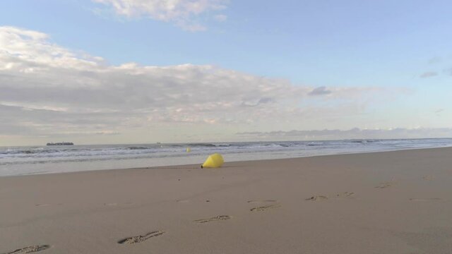 A lone yellow buoy resting on a sandy beach as gentle waves wash ashore, North Sea, Belgium coast, aerial