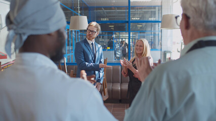 Back view of cafe staff watching young manager welcoming new employee with handshake