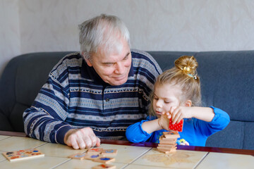 Naklejka premium Beautiful toddler girl and grandfather playing together pictures memory table cards game at home. Cute child and senior man having fun together. Happy family indoors