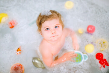 Cute adorable baby girl taking foamy bath in bathtub. Toddler playing with bath rubber toys....