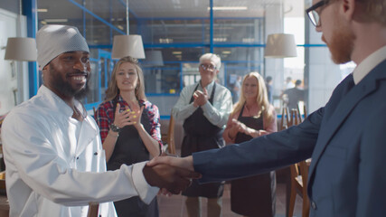 Close up of cafe owner shaking hands and congratulating african chef with promotion