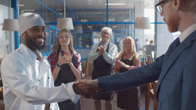 Close up of cafe owner shaking hands and congratulating african chef with promotion