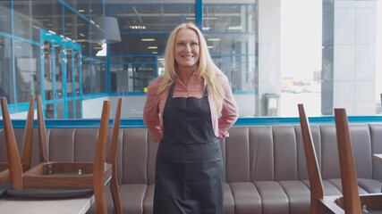 Senior happy cafe owner woman tie apron preparing to welcome guests in new cafe