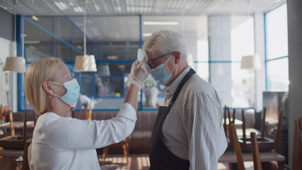 Senior manager of restaurant checking body temperature of staff with thermal imaging device