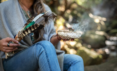 Woman holding a smudging wand and incense in a forest
