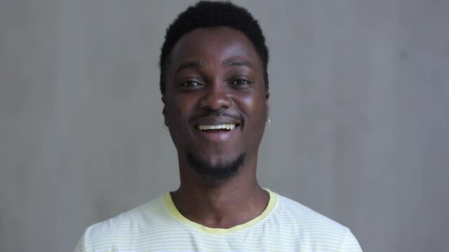 portrait of relaxed young black guy starting smiling and laughing when look at camera Spbi. happy handsome bearded man on grey background. casual clothing white shirt concept
